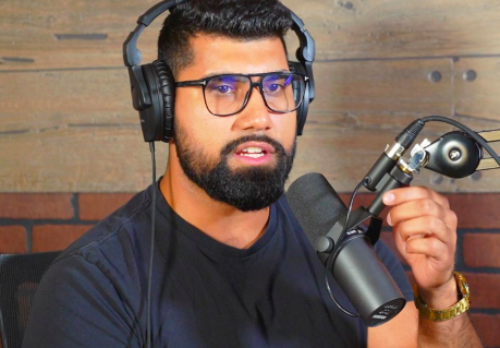 A photo of a man in a black shirt recording a podcast.