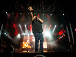 Luke Combs performs at Bluesfest. He sings into the microphone with his hand raised in the air.