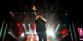 Luke Combs performs at Bluesfest. He sings into the microphone with his hand raised in the air.