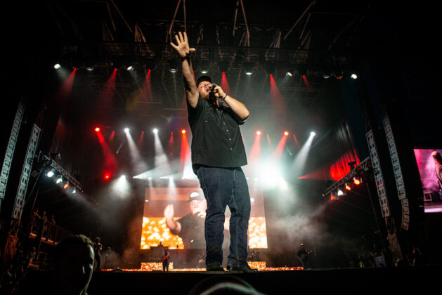 Luke Combs performs at Bluesfest. He sings into the microphone with his hand raised in the air.
