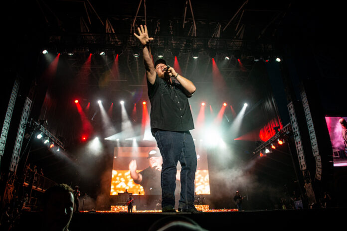 Luke Combs performs at Bluesfest. He sings into the microphone with his hand raised in the air.