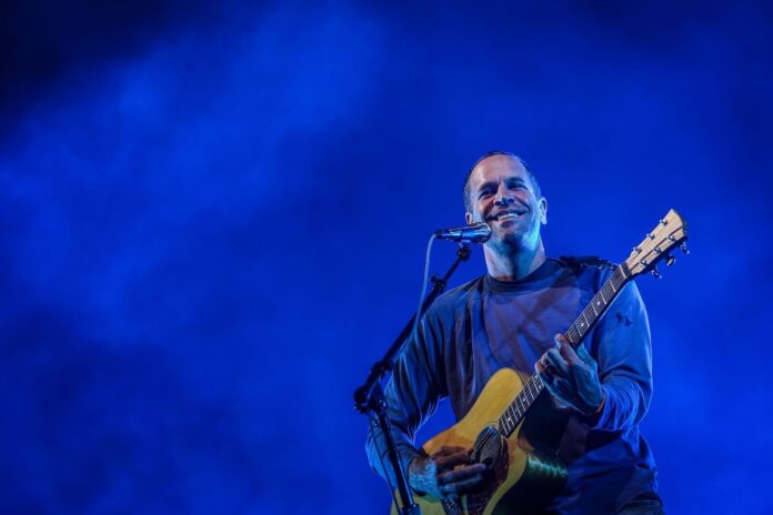 Jack Johnson performs at Bluesfest. He is smiling at the crowd, holding an acoustic guitar.