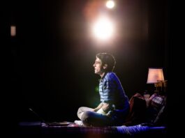 Anthony Norman as Evan Hansen sits on his bed looking out into the audience.