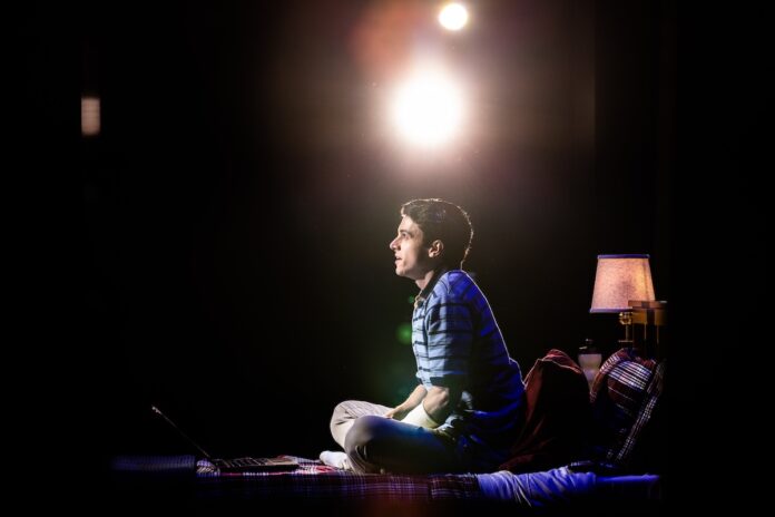 Anthony Norman as Evan Hansen sits on his bed looking out into the audience.