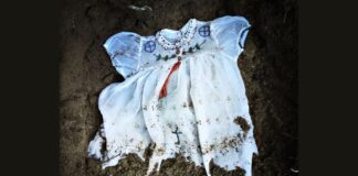 A Christian baptism gown with Indigenouss beadwork lies in the dirt.
