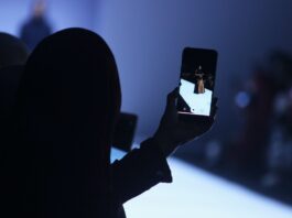 Person holding an phone camera. Image on the phone displays a model walking on the runway.