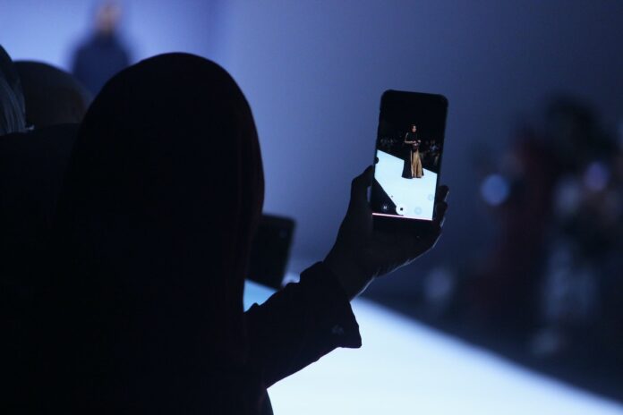Person holding an phone camera. Image on the phone displays a model walking on the runway.