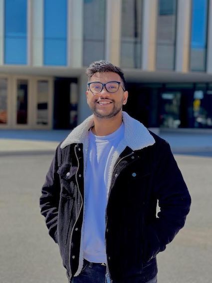 Faris Riazudden smiles at the camera standing outside of Nicol building