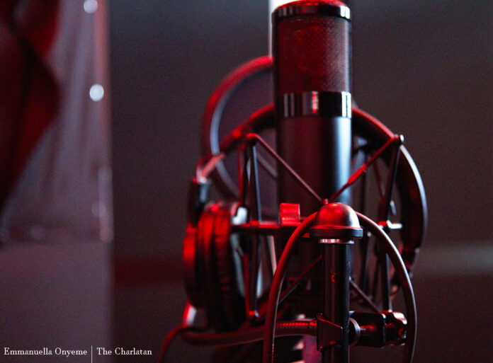 A microphone with headphones draped around it at Cave Recording Studios behind a dark background.