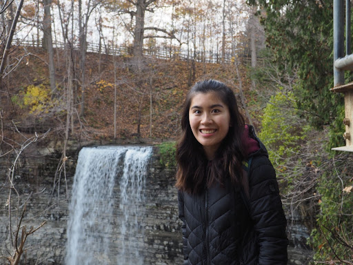 Cynthia Ling smiles at the camera in a warm jacket with a waterfall behind her