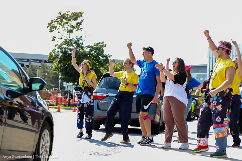 People wearing blue and yellow shirts cheering as cars pass by.