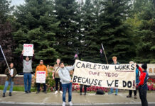 Opinion: In the aftermath of Bill 28, we must stand up for workers’ rights Several people standing outside holding signs and a banner with green trees in the background.