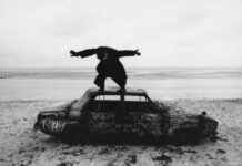 Review: The 1975’s ‘Being Funny in a Foreign Language’ avidly explores modernity and loneliness Album cover for The 1975's new album. Black and white image of Matty Healy standing on top of a car with his hands spread out.
