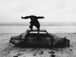 Album cover for The 1975's new album. Black and white image of Matty Healy standing on top of a car with his hands spread out.