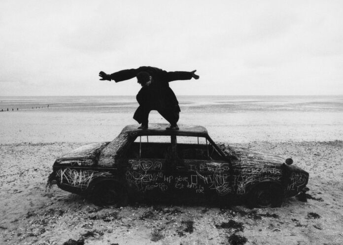 Album cover for The 1975's new album. Black and white image of Matty Healy standing on top of a car with his hands spread out.