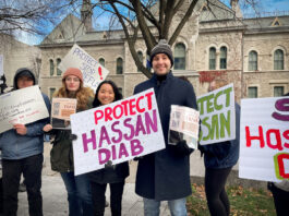 People standing smiling holding signs in support of Hassan Diab