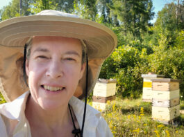 Dinah Robinson, owner of Bytown Bees, poses in front of her bee hives at her cottage