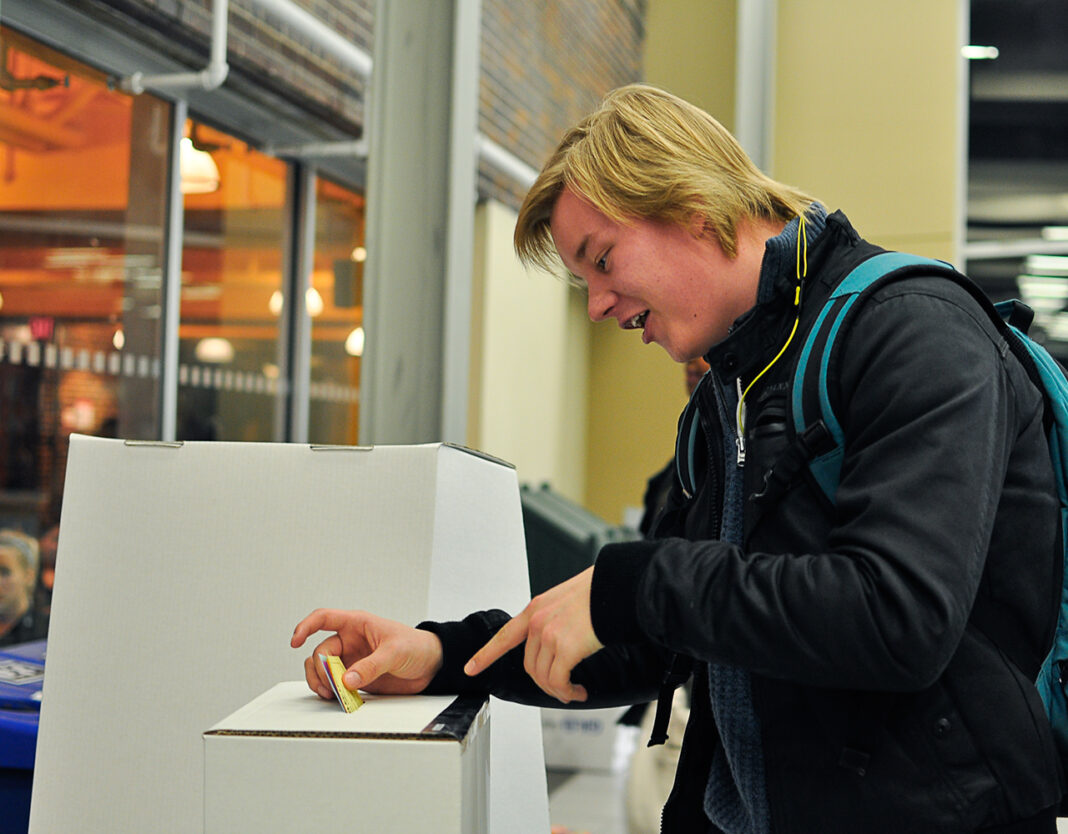 a white blonde man puts his ballot at a voting center.