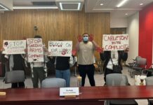 Student activists call for divestment, ask for Carleton’s stance on peaceful protest Students hold signs reading "stop funding arms companies" "blood on your hands" and "Carleton you're complicit" while holding up their red-painted hands.