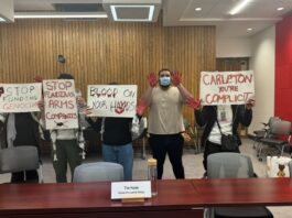 Students hold signs reading "stop funding arms companies" "blood on your hands" and "Carleton you're complicit" while holding up their red-painted hands.