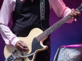 Close up shot of a man strumming a yellow guitar on stage. Pic is just of his hands and the guitar.