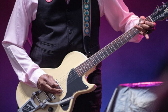 Close up shot of a man strumming a yellow guitar on stage. Pic is just of his hands and the guitar.