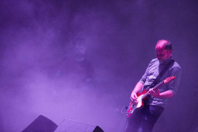 Purple background smoke with man playing guitar on stage.