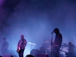 Blue background smoke reveals 3 man playing guitar on stage.