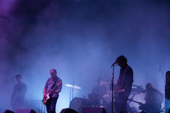 Blue background smoke reveals 3 man playing guitar on stage.