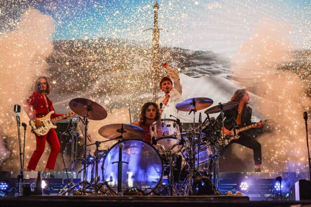 With white sparkles going off on stage, a band rocks out on stage.