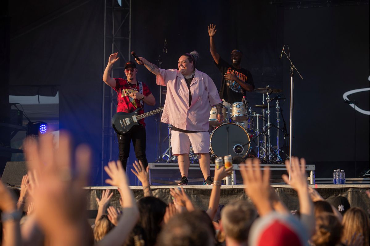 Lady with a pink button down shirt points the mic to the crowd and sings with them on stage. 