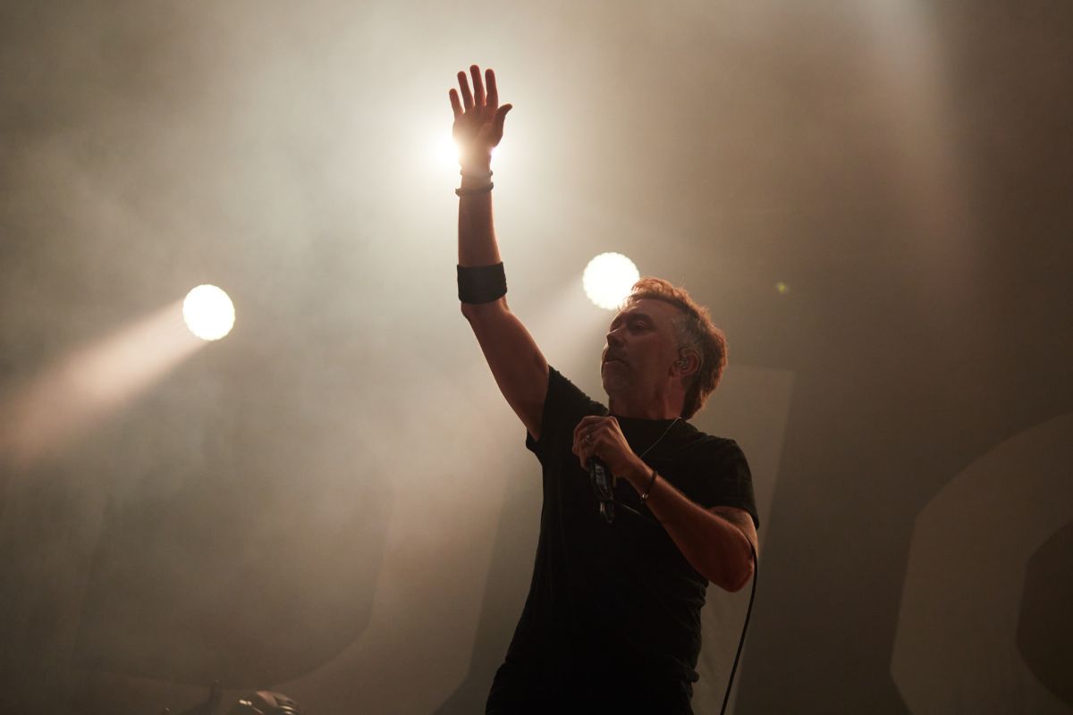 Man in a black shirt raises is arm on stage. 