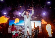 Review of CityFolk Day Two: A night of electrifying rock ‘n’ roll With flames going off at the side of the stage, the lead singer in an all-white bedazzled outfit sings with his band on stage.