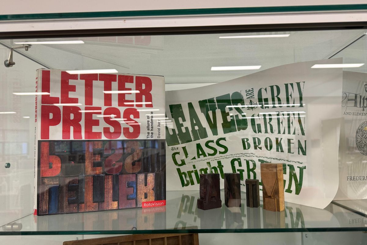 In a glass case, a letter pressing book is featured along with letter pressing art. 