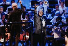 Review: Norm Lewis delivers ‘Big Broadway’ with big hits, bigger performance A Black man in a suit sings with his right hand extended in the air in passion. In the back, the NAC orchestra is seated and playing along.