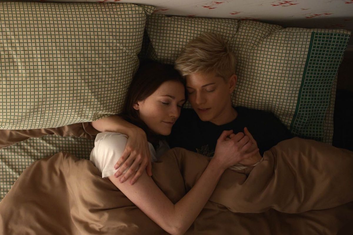 On a bed, two women lovingly cuddle and hold each other. 