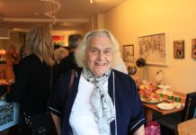 Trans activist Joanne Law celebrates 80th birthday An elderly woman wearing a white blouse with a blue floral scarf smiles for the camera.