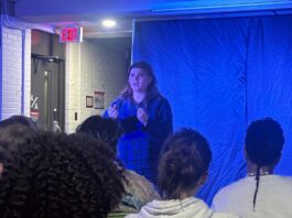 Amid a blue background and a crowd watching, a girl in a blue bottom down shirt acts out a scene from The Edge of Seventeen.