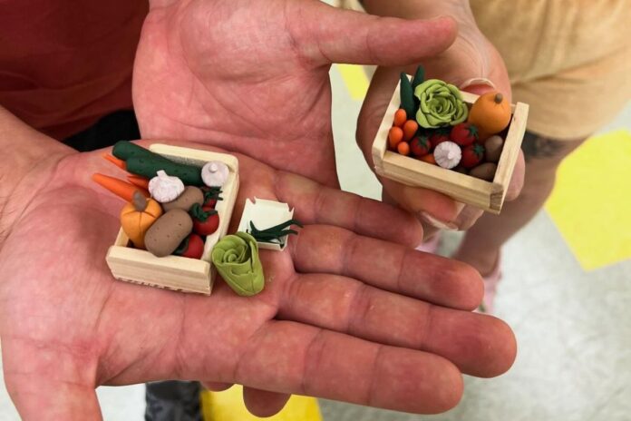 Close up of two hand palms with small clay vegetables in the middle.