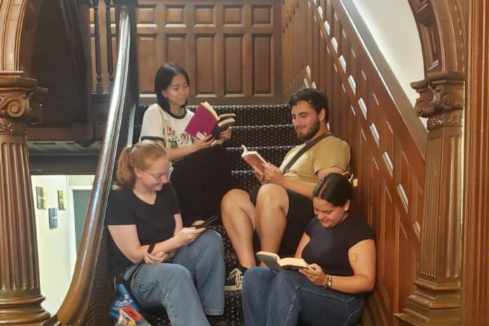 Sitting on an old wooden staircase, four people, 3 girls and one man, read books.