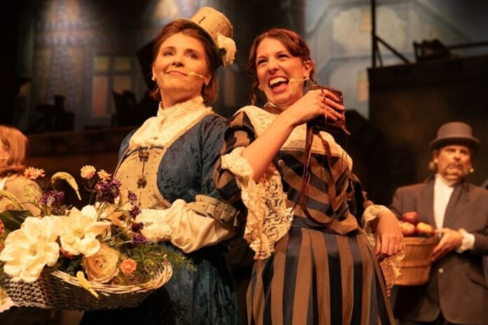 Two women of the ensemble, one in a blue 1700s dress the other in a brown and black 1700s dress.