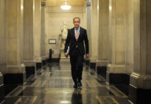 A man in a suit walks down a hallway.