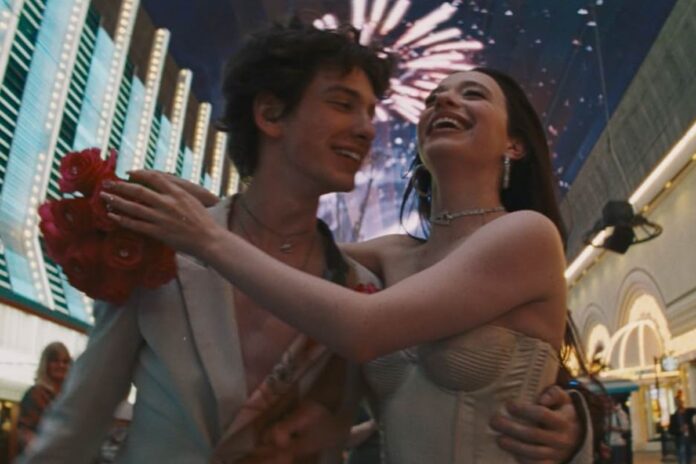 A man and a woman wearing white in an embrace with fireworks and lights in the background.