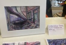 Visual Arts Carleton’s first-ever market aims to grow student arts community On a white display table, a purple watercolour of an architecture building is displayed with a sign that reads "Watercolour prints."