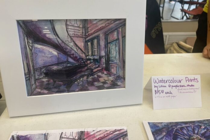 On a white display table, a purple watercolour of an architecture building is displayed with a sign that reads 