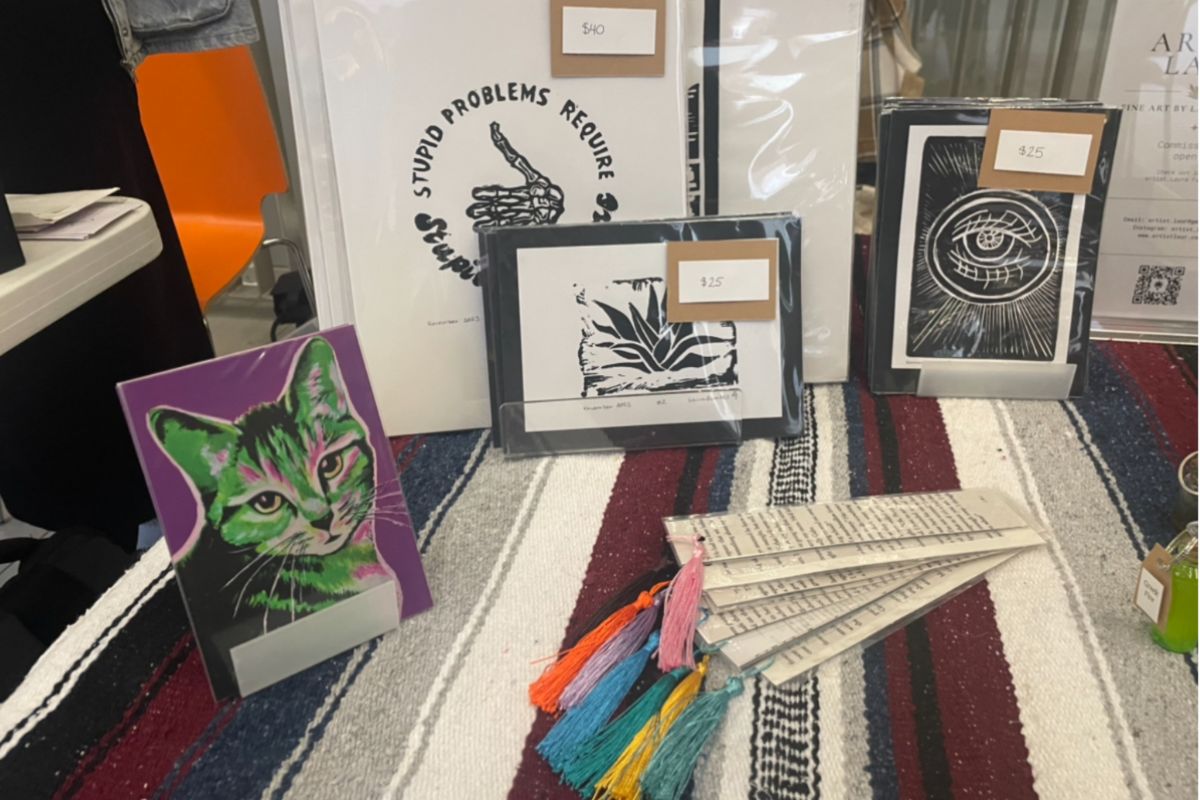 On a display table, there are colourful bookmarks, a green print of a cat, and a black and white print. 