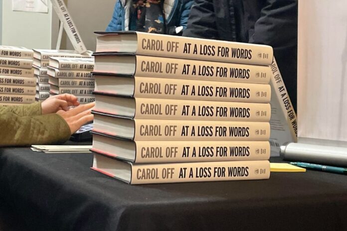 Copies of Carol Off’s new book, 'At A Loss For Words: Conversation in the Age of Rage,' sit on a table at Southminster Church in Ottawa. The spines of the books are all piled up on top of each other with a hand reaching out to sign a copy.