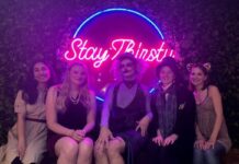 ‘Drag Me To Trivia’ embraces queer performances on campus Behind a neon pink sign that says "Stay Thirsty" five people sit and smile at the camera. They are dressed in various Halloween costumes