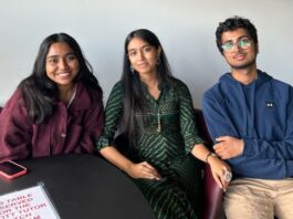 Sitting down at a black table, three Hindu Students' Society members smile for a photo.