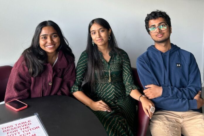 Sitting down at a black table, three Hindu Students' Society members smile for a photo.